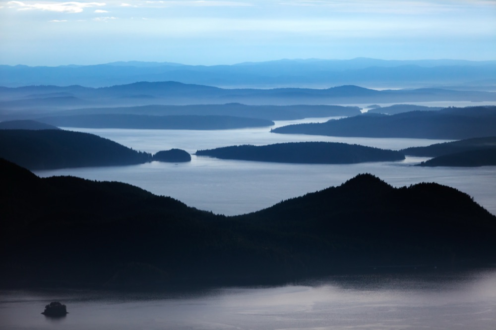 Layered forested islands and calm channels of Puget Sound receding into blue haze at dusk.